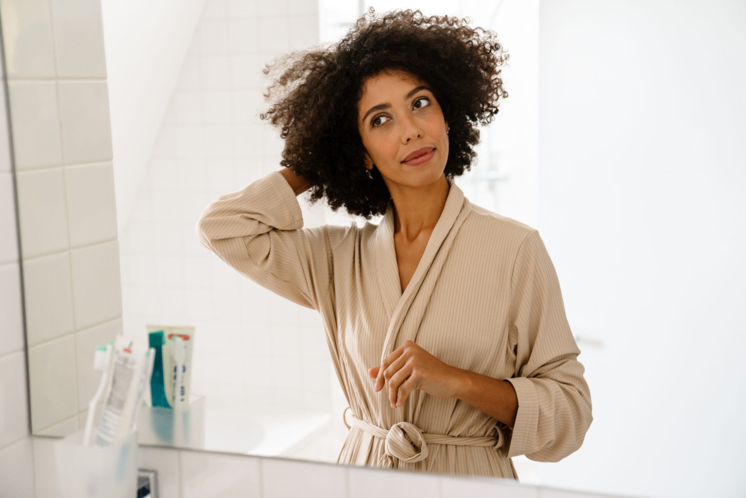 African american young woman smiling and looking in mirror at bathroom